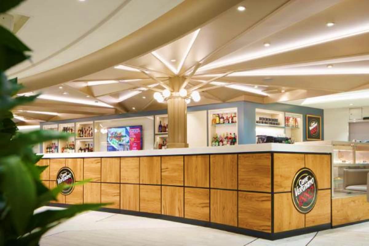 Modern bar counter with wooden panels and illuminated shelving displaying bottles, featuring ornate ceiling with geometric li