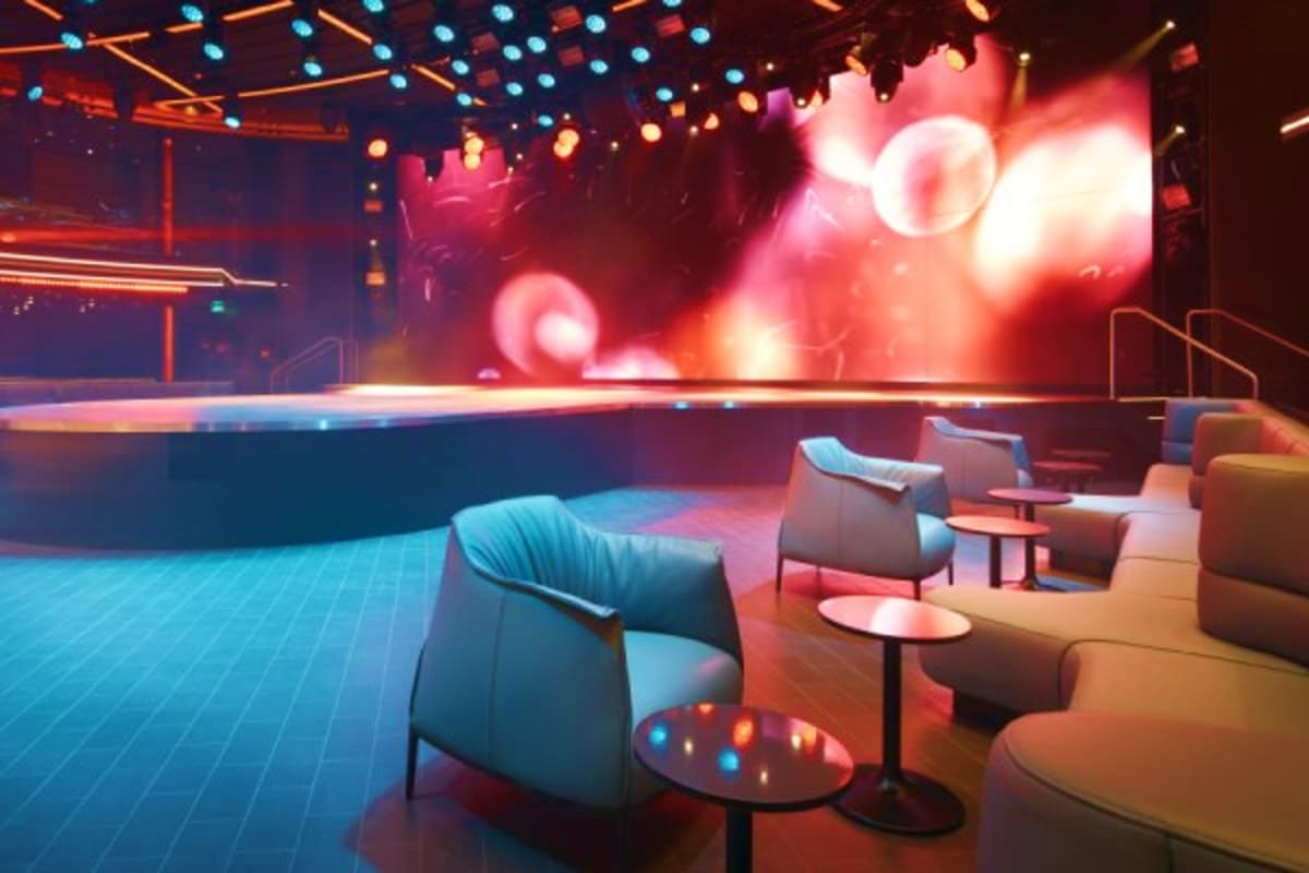 Modern nightclub interior with lounge seating, glowing neon lights in red and blue, and large illuminated backdrop display wi