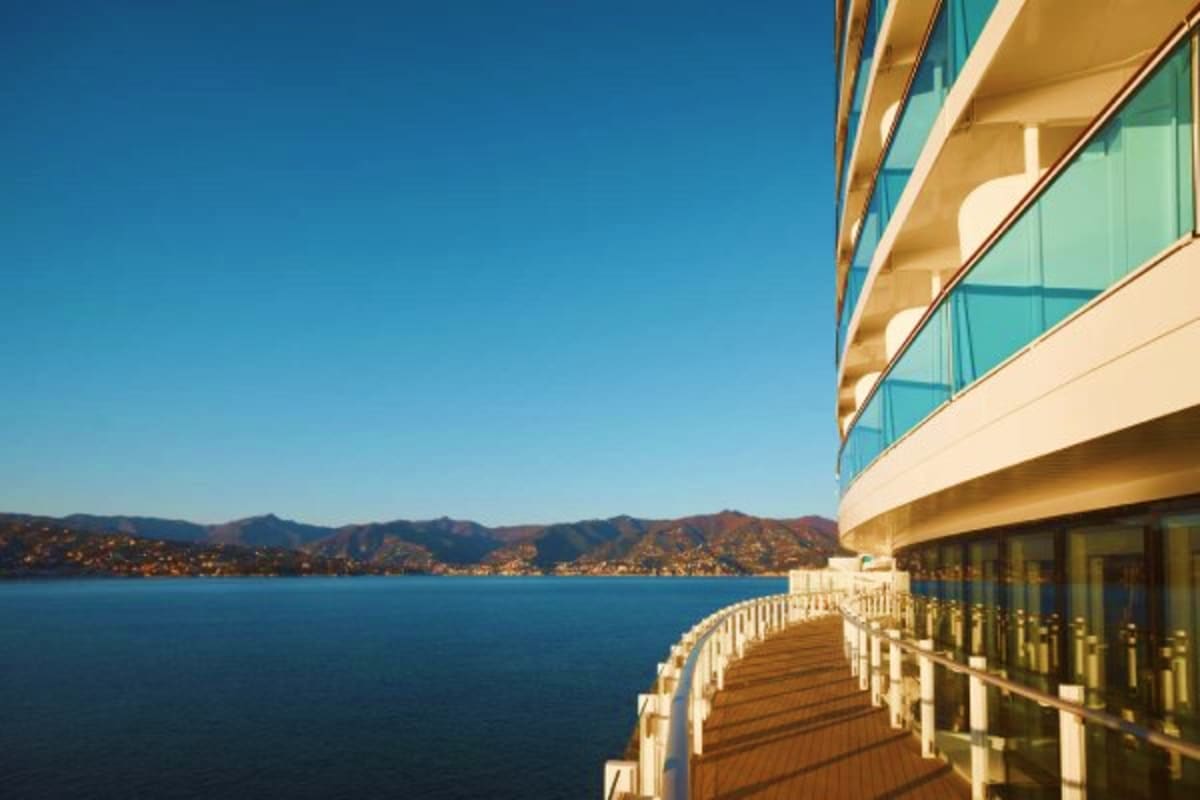 Curved wooden deck of luxury cruise ship with glass railings overlooking blue Mediterranean sea and coastal mountains