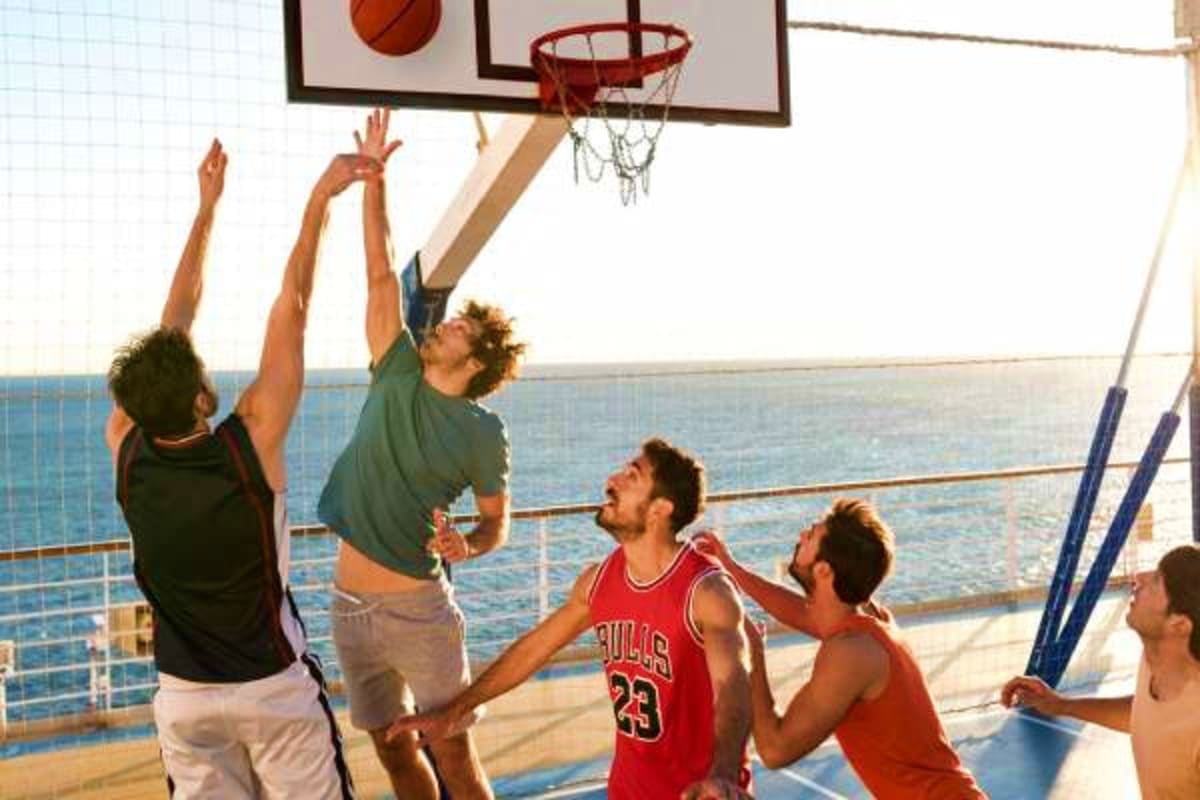 Group of men playing basketball on a cruise ship deck with ocean and railing visible in background