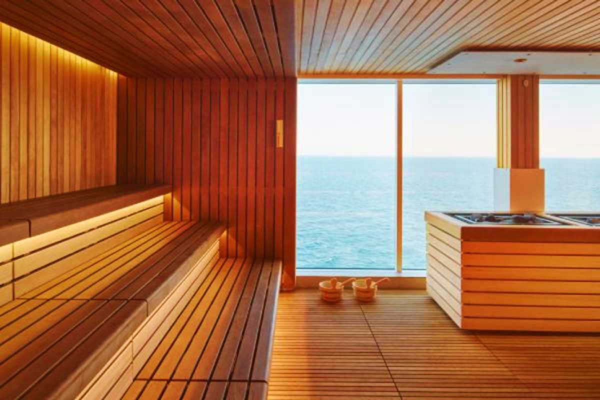 Modern sauna with wooden benches and walls overlooking calm ocean waters through floor-to-ceiling windows