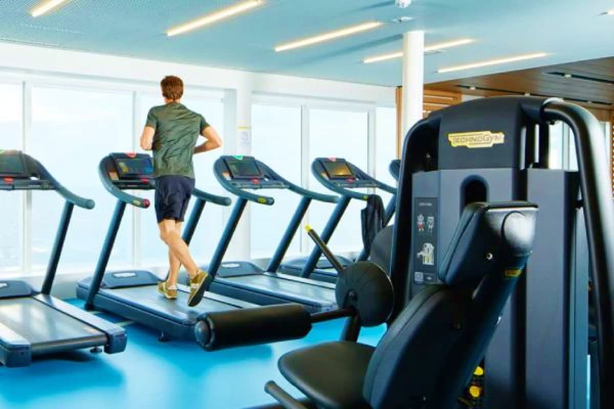 Man running on treadmill in modern gym with multiple fitness machines and blue flooring