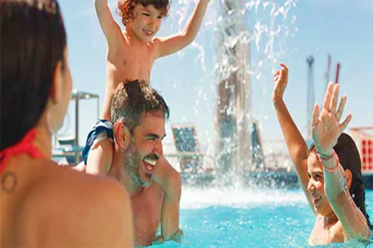 Family enjoying water splash at pool on cruise ship with ocean and port in background