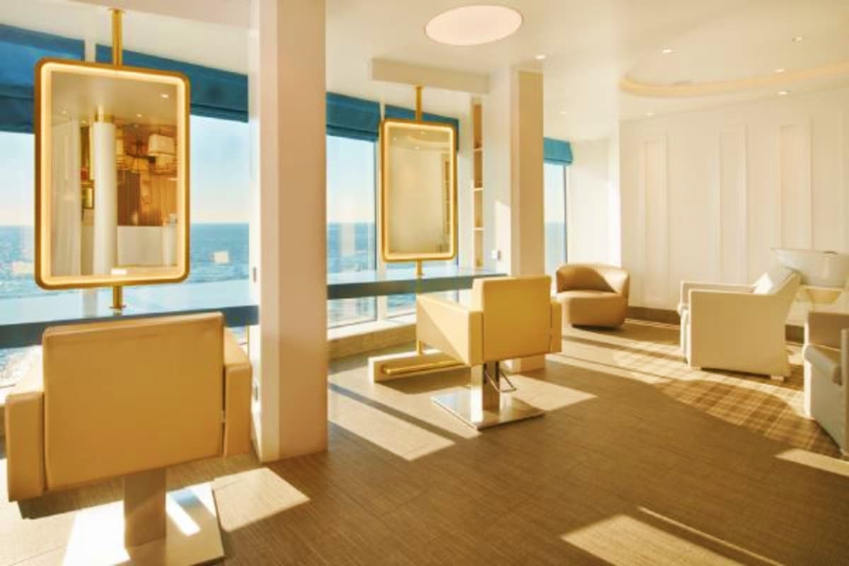 Modern luxury spa interior with gold-framed mirrors, beige furnishings, and ocean views through floor-to-ceiling windows