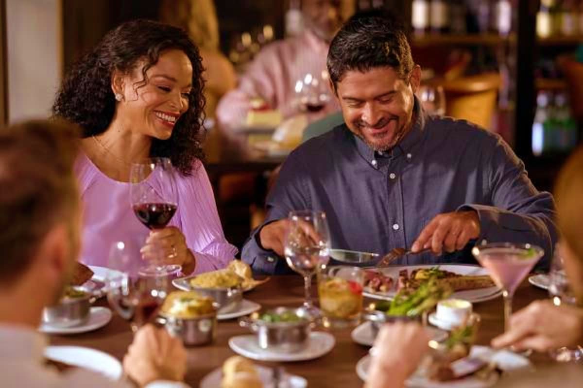 Couple dining at restaurant table with wine and food during cruise ship dinner event with other guests in background