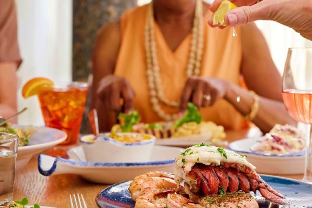Family enjoying Mediterranean lunch with grilled meat and seafood dishes, wine, and fresh citrus at outdoor dining table