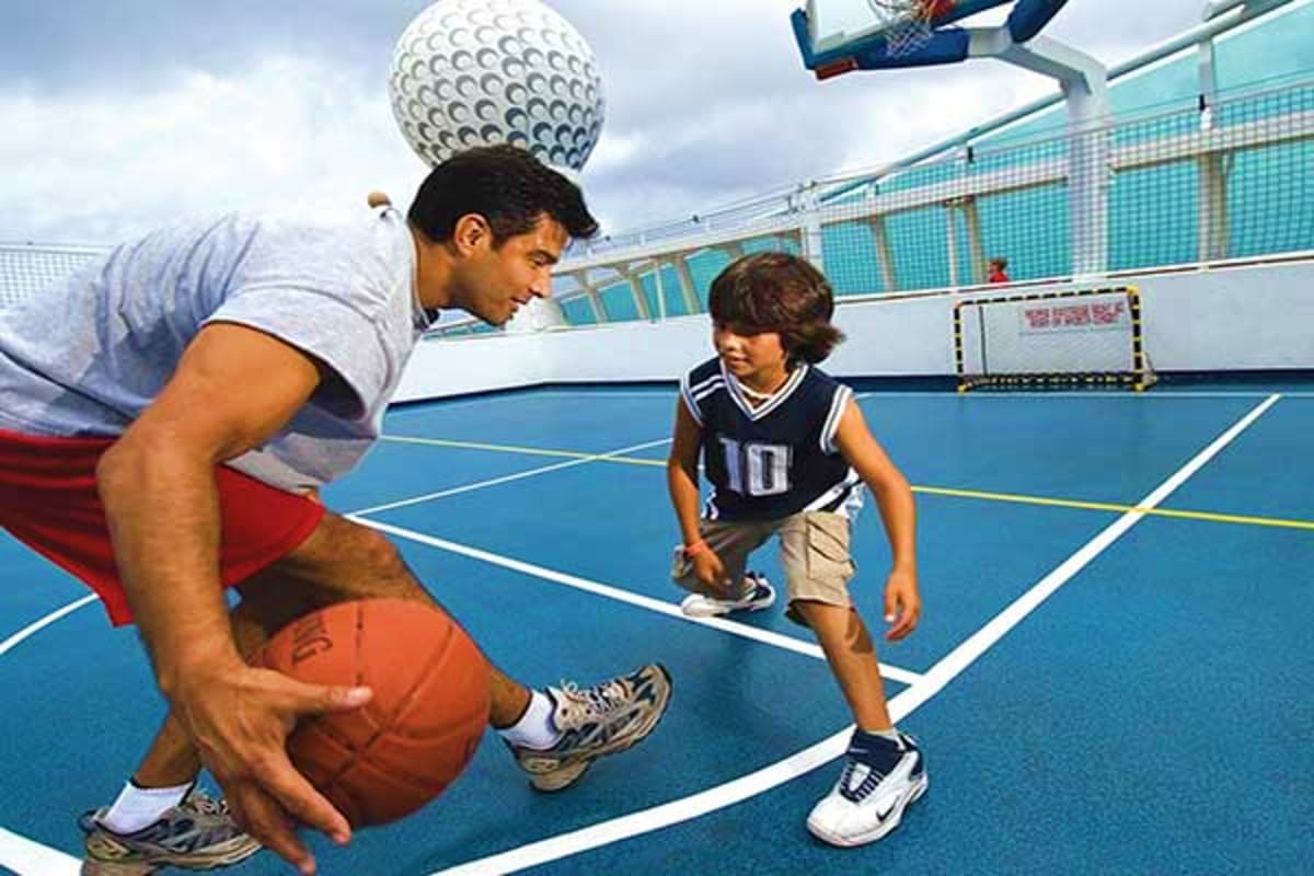 Adult teaching child basketball and volleyball on outdoor cruise ship sports court