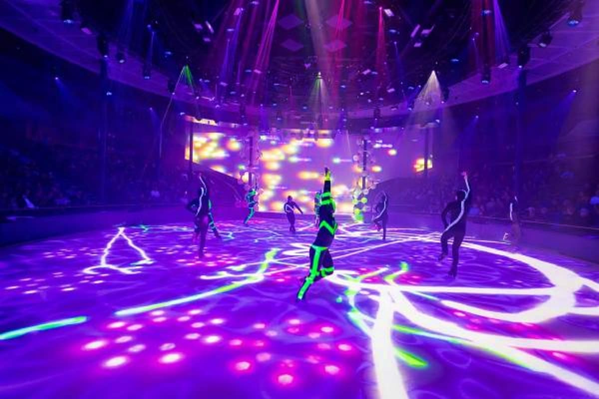 Performers in neon green costumes dancing on illuminated purple and pink dance floor in modern cruise ship nightclub venue wi