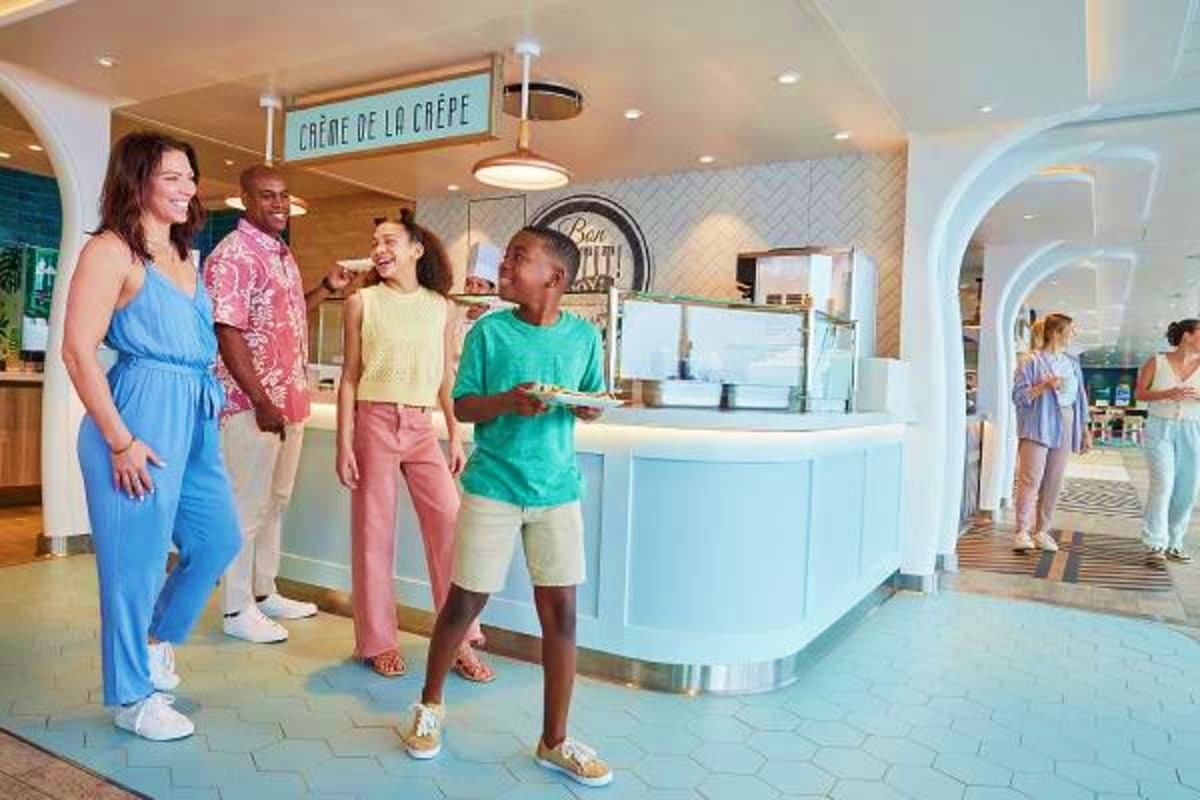 Families enjoying Crème de la Crêpe café on a cruise ship with light blue curved counter and signage overhead