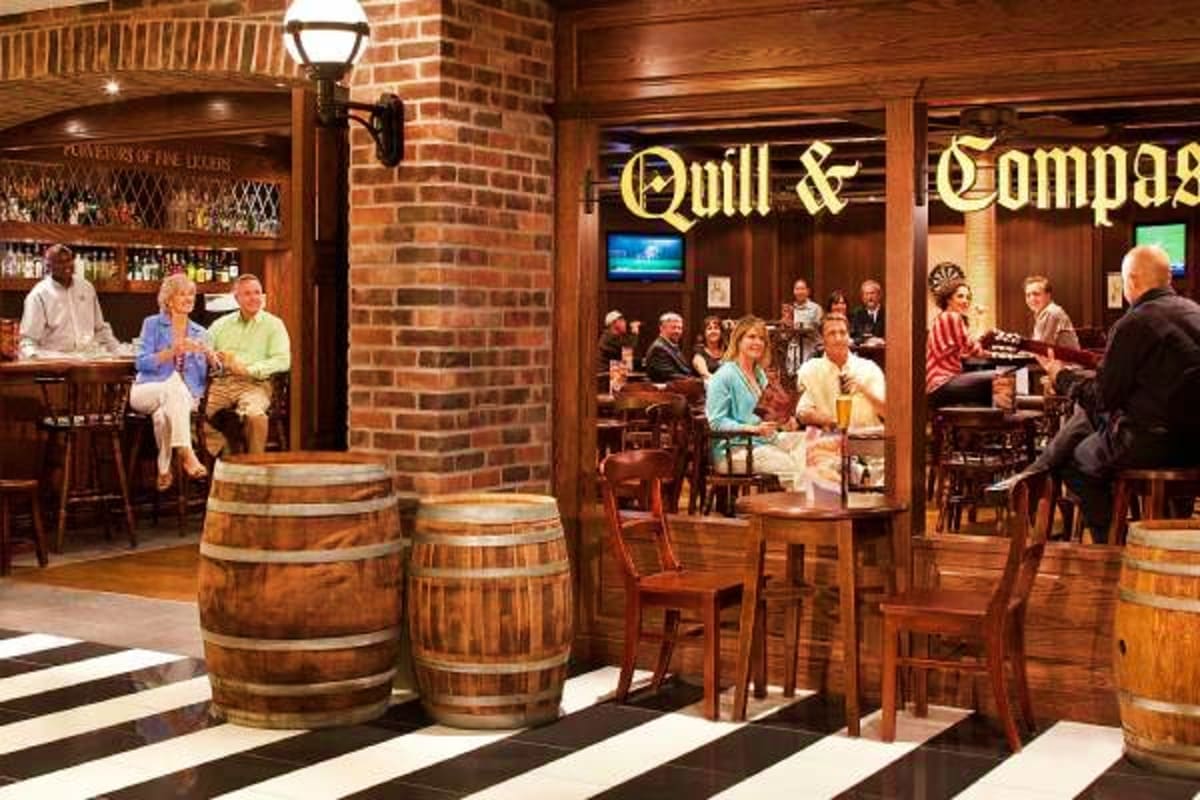 Interior of Quill & Compass bar on cruise ship with wooden barrels, brick walls, and passengers enjoying drinks and socializi