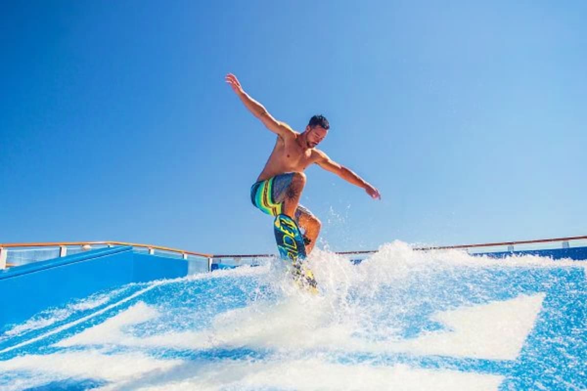 Man surfing on artificial wave at cruise ship FlowRider water park attraction under clear blue sky