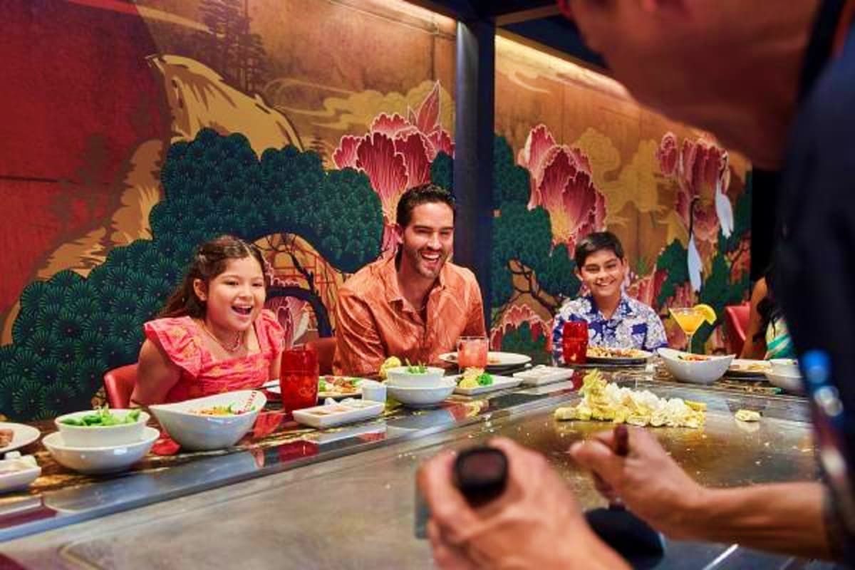 Family dining at teppanyaki restaurant with chef cooking at table, colorful Asian-inspired mural backdrop