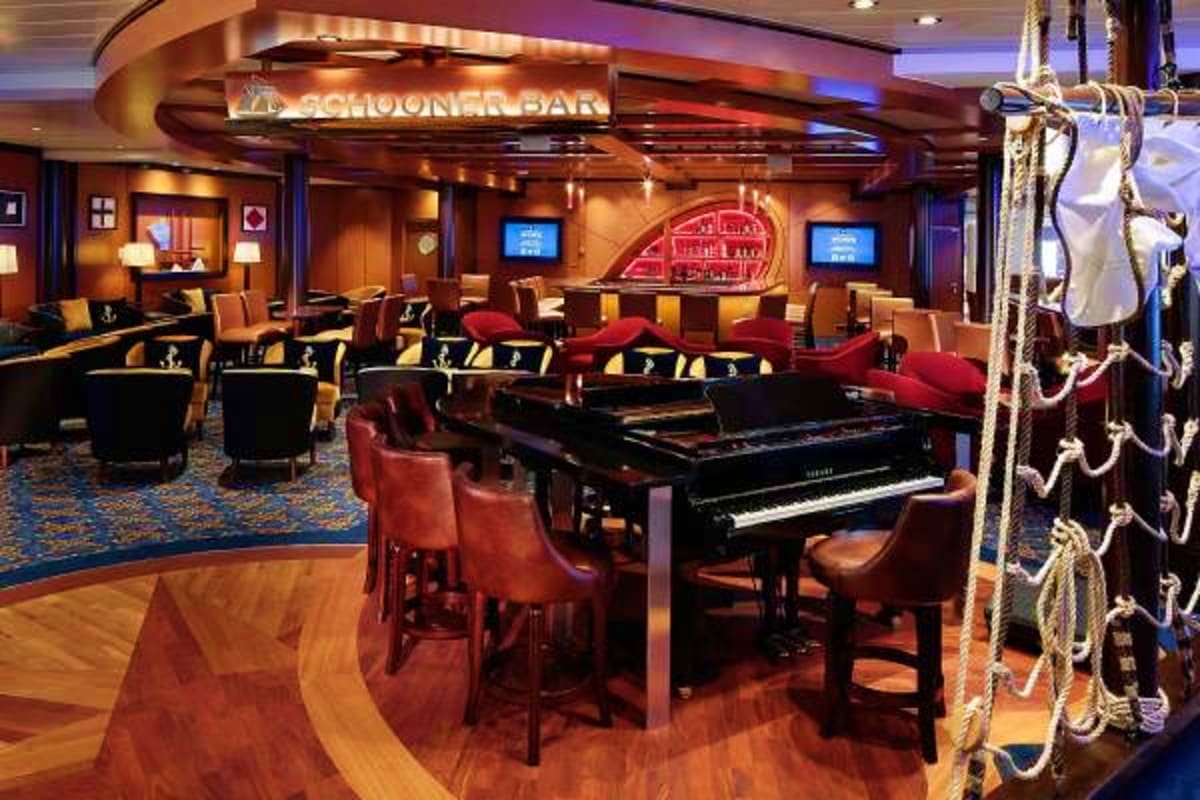 Schooner Bar lounge on cruise ship with grand piano, red seating, neon sign, and nautical rope decor