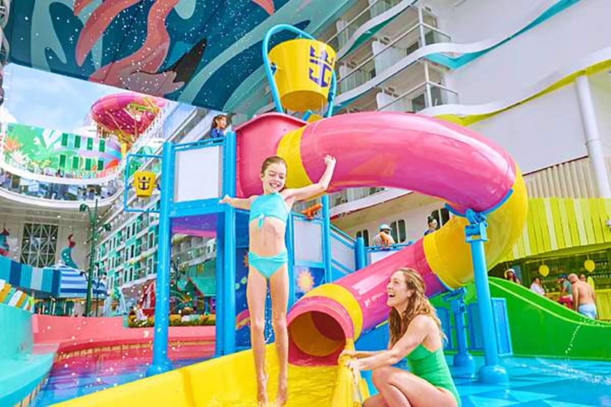 Children playing on a colorful indoor water slide and splash pool area on a cruise ship