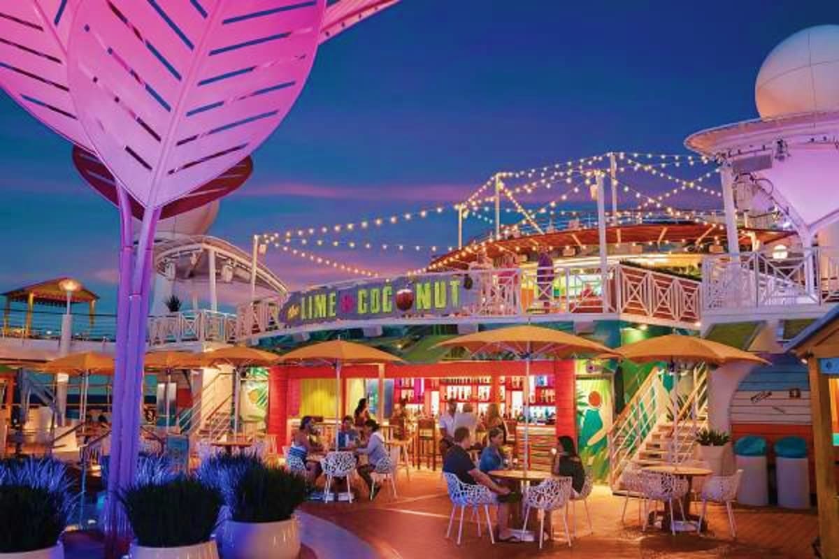 Illuminated outdoor dining and bar area on cruise ship deck at dusk with colorful signage and string lights