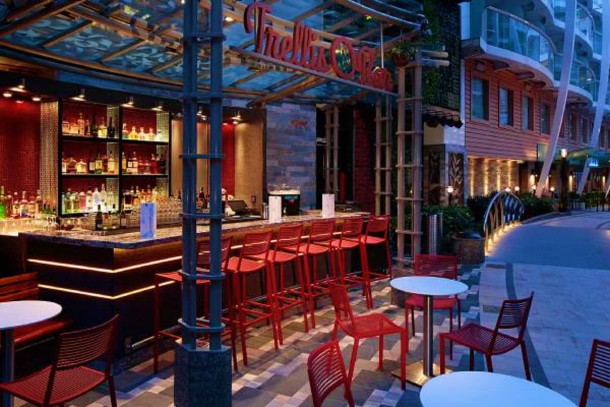 Modern rooftop bar with red chairs, illuminated liquor shelves, and evening city views in urban setting