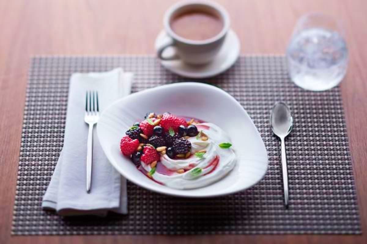 Fine dining plated dessert with fresh berries and cream on white plate with coffee cup and water glass on dark placemat