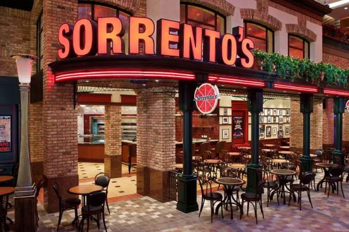 Sorrento's Italian restaurant storefront with red neon signage, brick facade, outdoor seating, and grapevine decoration on cr