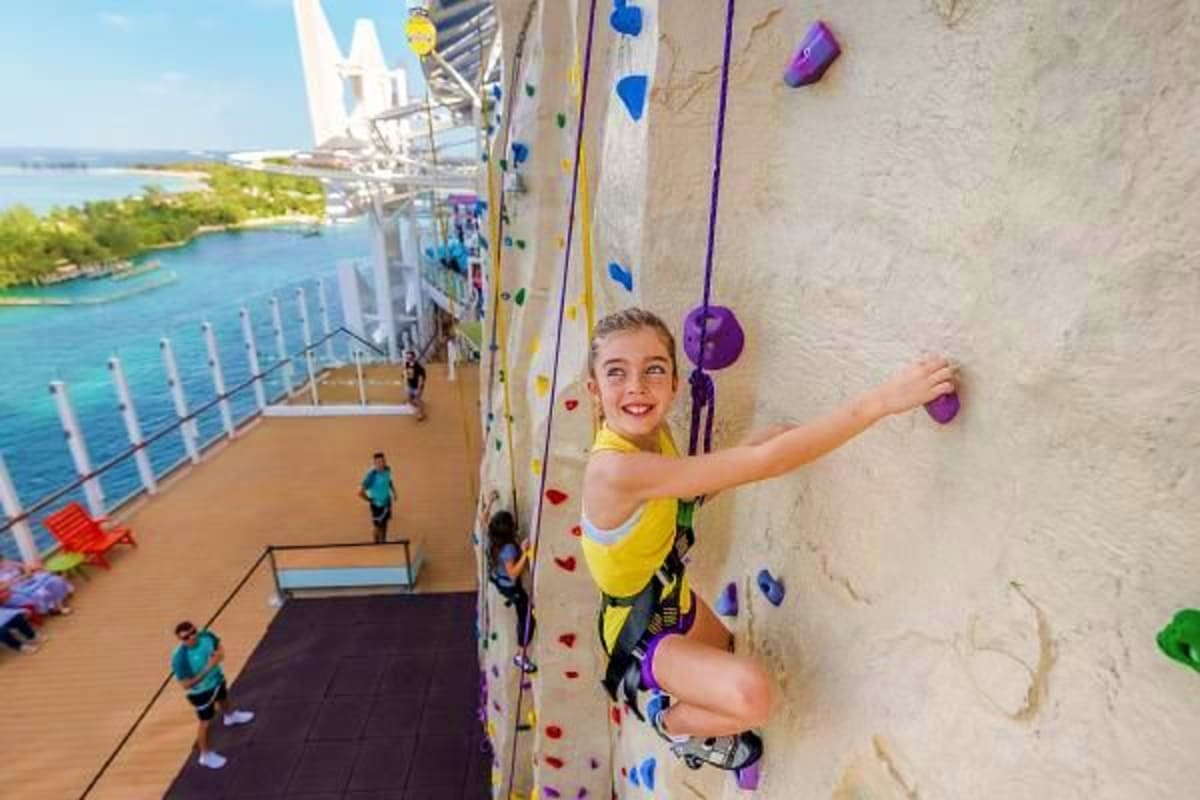 Child rock climbing on cruise ship wall with ocean and coastline visible in background