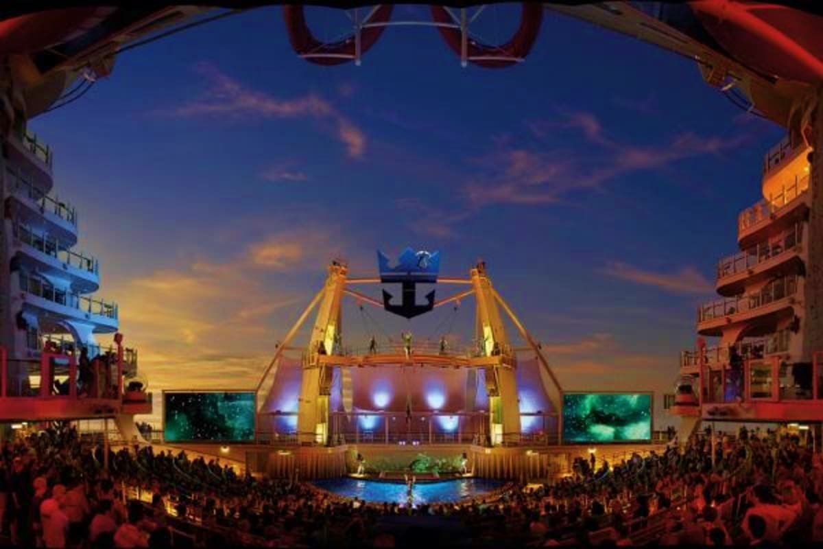 Illuminated stage with golden cables and blue anchor logo on cruise ship at night, surrounded by audience in theater venue