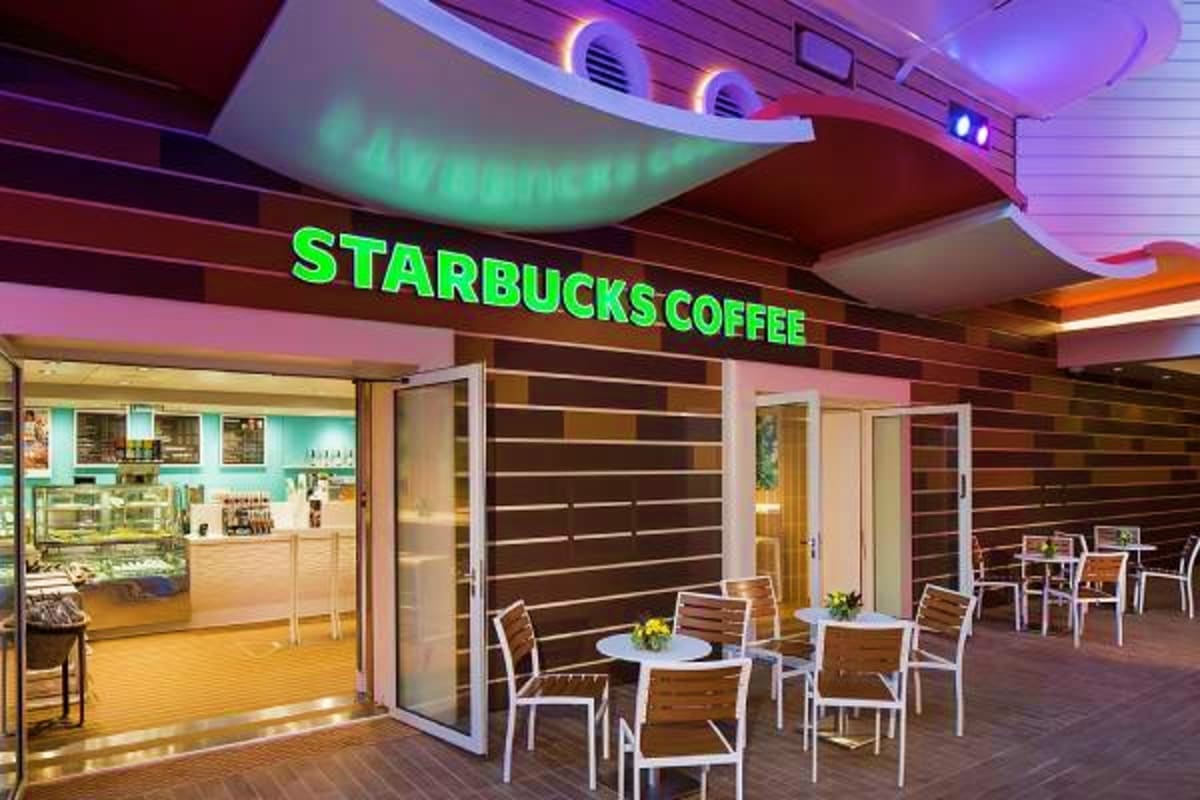 Starbucks Coffee shop interior on a cruise ship with green neon sign, seating area with white chairs and tables, and modern l