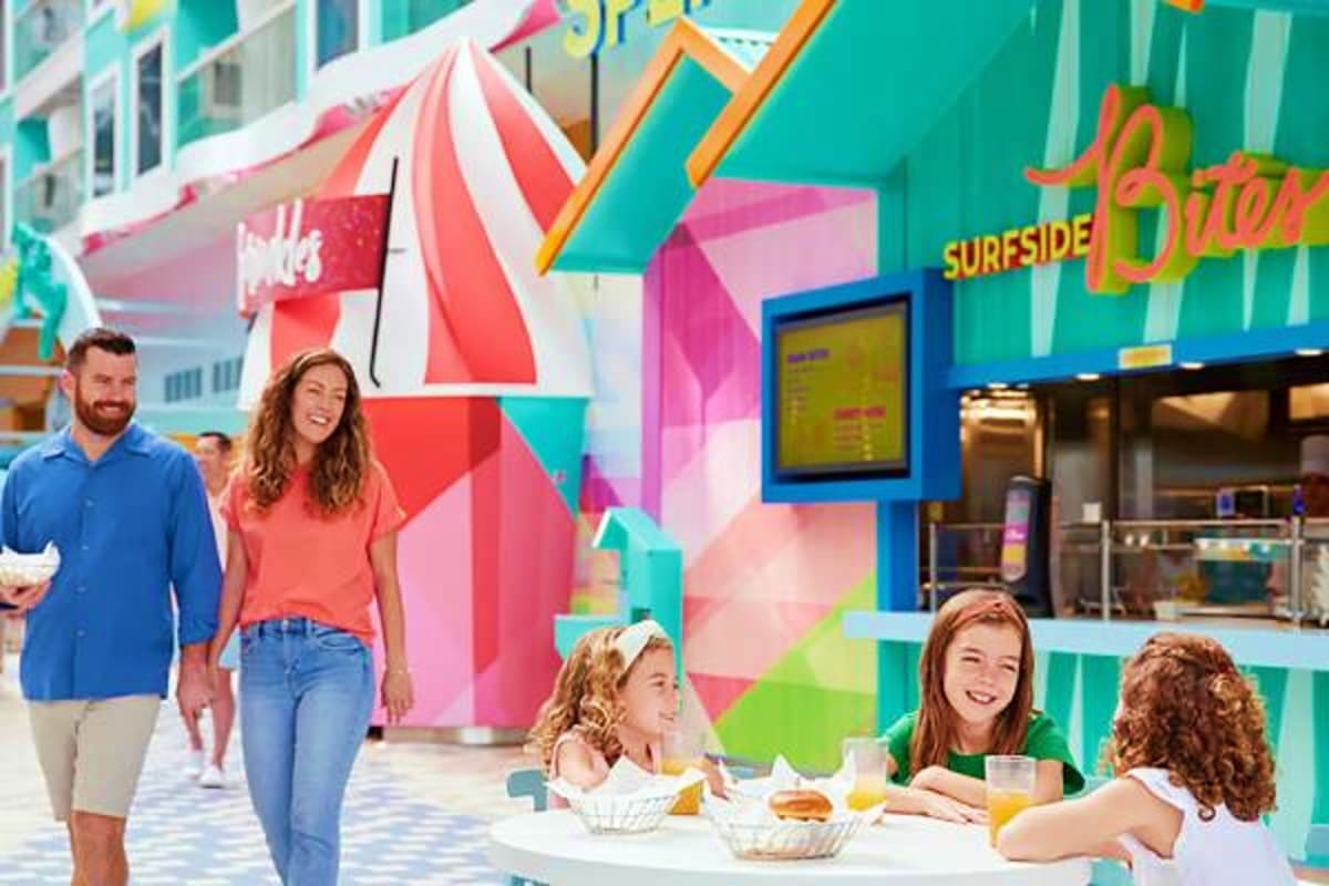 Colorful seaside promenade with families dining and walking near a vibrant "Surfside Sitter" storefront with red and white st