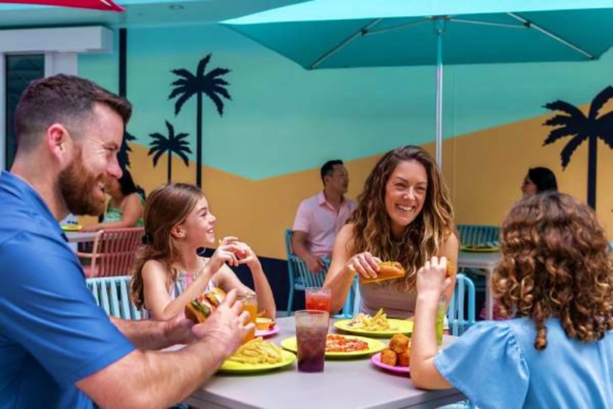 Family dining at outdoor poolside restaurant with turquoise umbrella and tropical beach mural decor