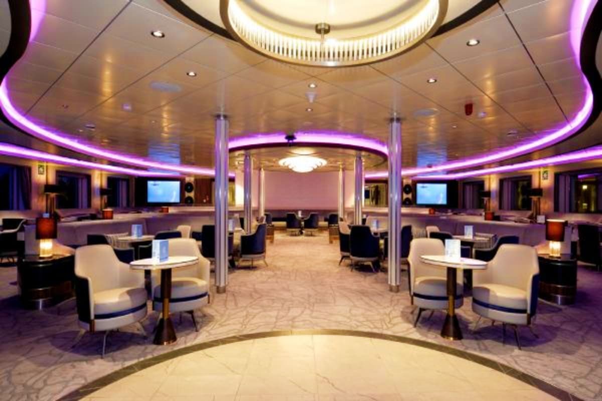 Arctic Expedition with Quark Expeditions aboard Ocean Explorer Modern cruise ship lounge with purple ambient lighting, white armchairs, round tables, and central columns
