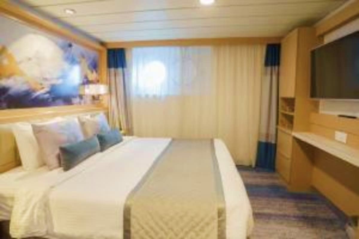 Arctic Wonders of Greenland and Iceland Luxury cruise ship stateroom with queen bed, porthole window, wooden furnishings, and modern décor