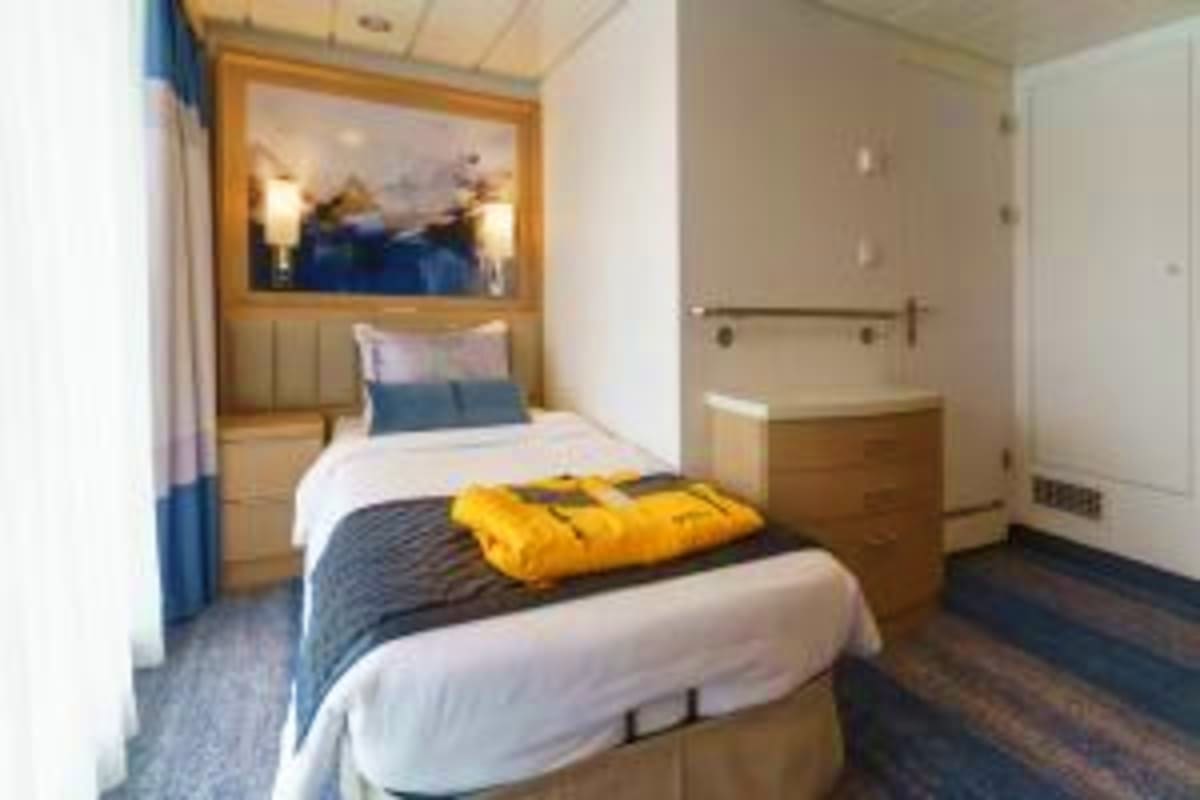 Arctic Explorer Expedition with Ocean Explorer Modern cruise ship cabin with queen bed, white bedding, yellow blanket, blue accent pillows, framed ocean artwork, and ensuit