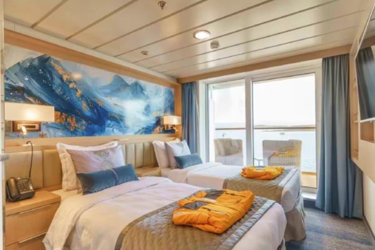 Arctic Expedition Voyage Luxury cruise ship cabin with two beds, mountain landscape artwork, ocean view balcony, and orange expedition parkas laid out