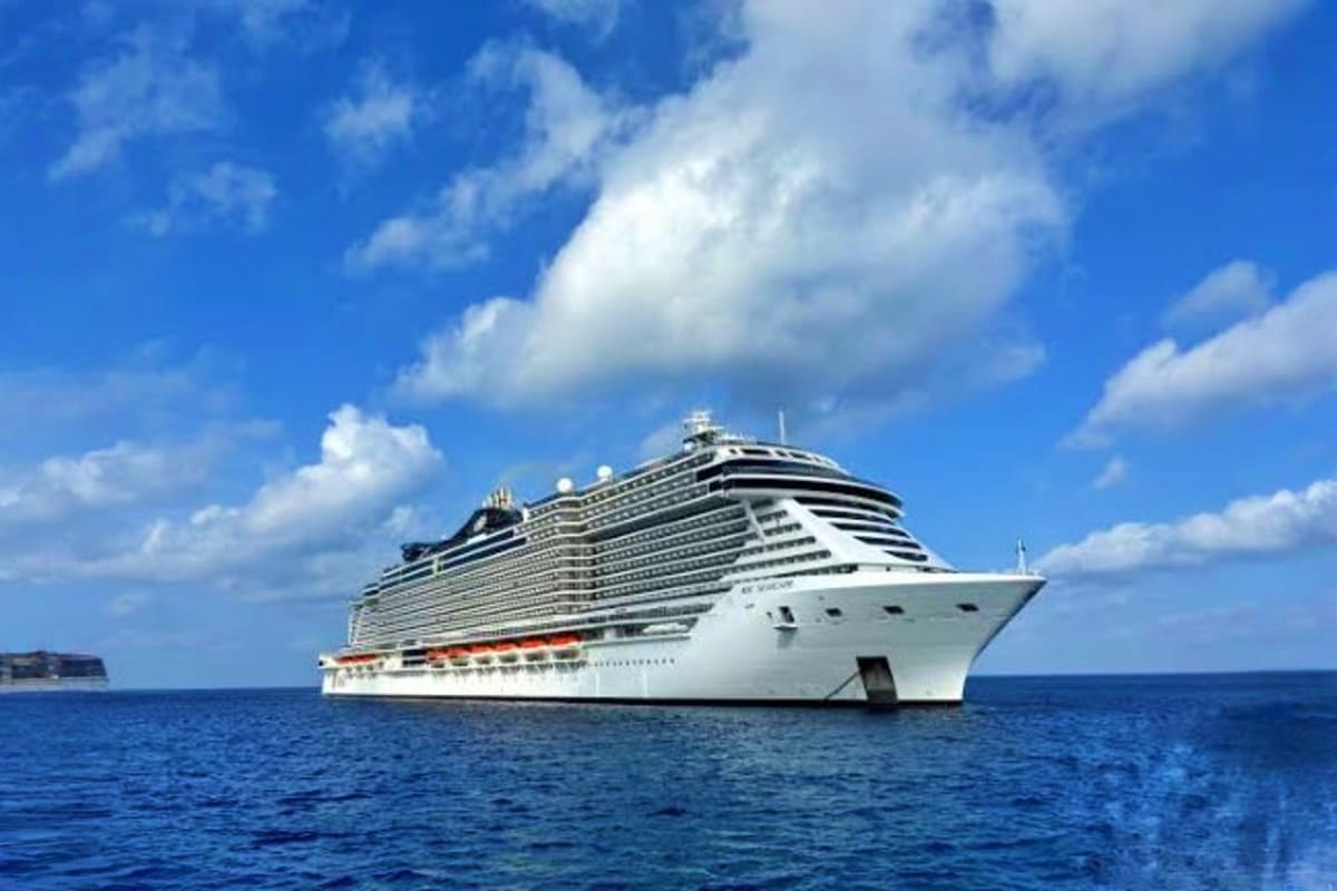 Greenland & Canada's Arctic Discovery Large modern cruise ship with white hull and red stripe sailing on blue ocean under clear sky with white clouds