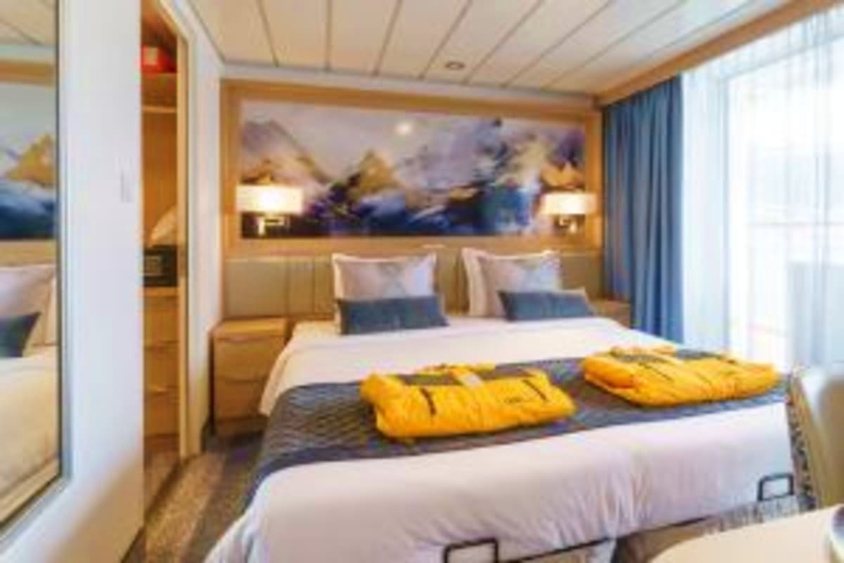 Greenland & Canada's Arctic Discovery Luxury cruise ship cabin with twin beds, yellow life jackets, mountain landscape artwork, and ocean view windows