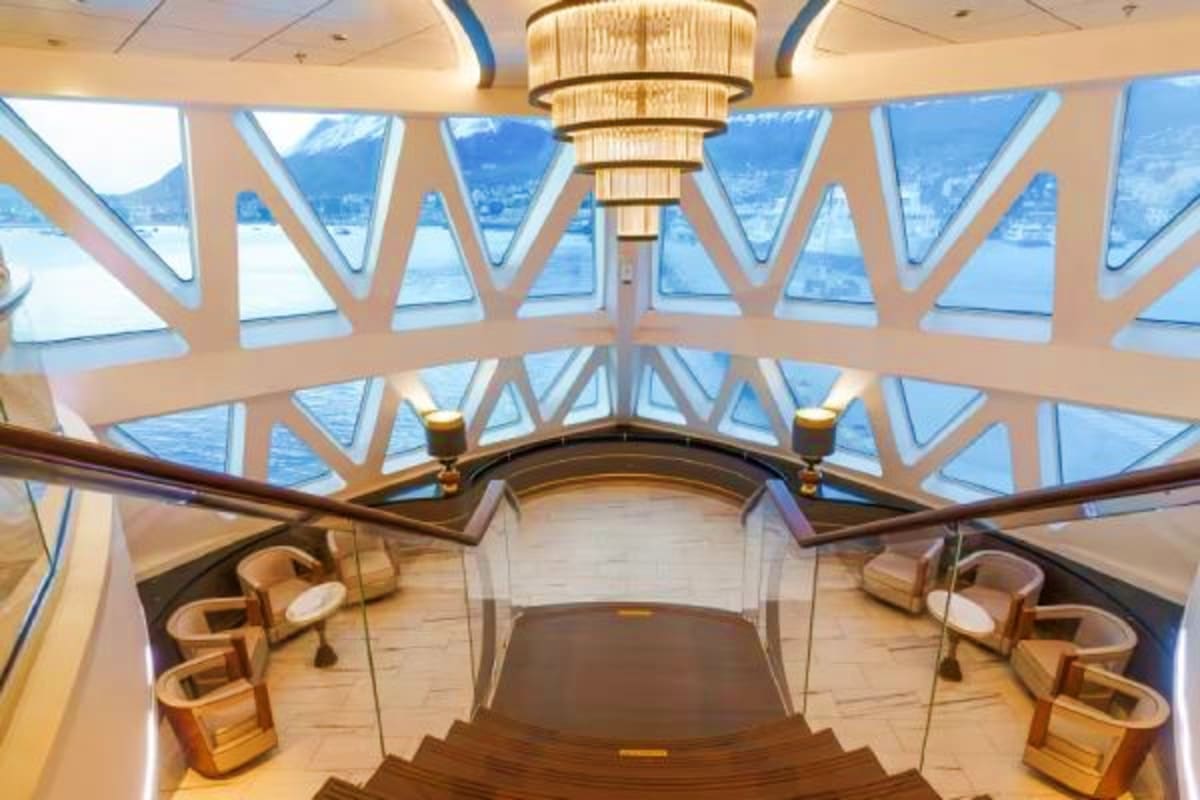 Greenland & Canada's Arctic Discovery Luxury cruise ship interior with panoramic ocean views through geometric windows, wooden deck, chandelier, and seating areas