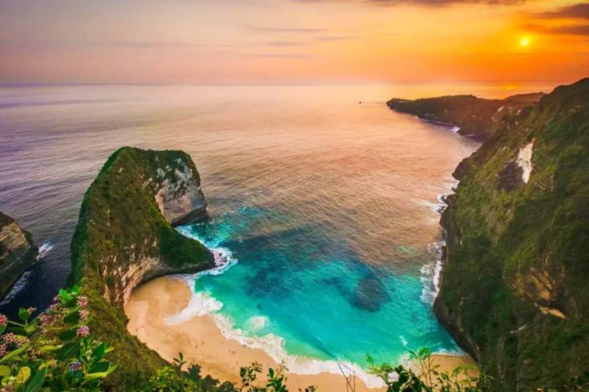 Kelingking Beach in Bali at sunset, featuring turquoise waters, white sand cove, lush green cliffs, and golden sky