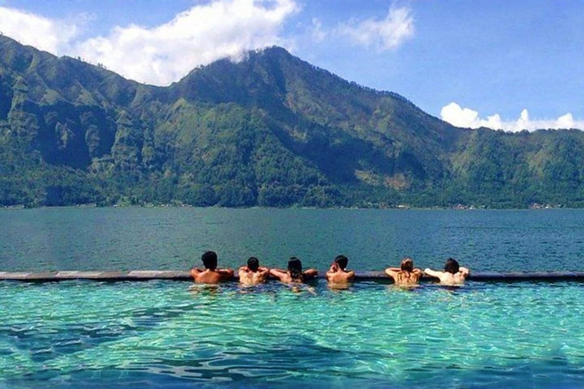 Group of people swimming in turquoise water with forested mountain backdrop in Bali