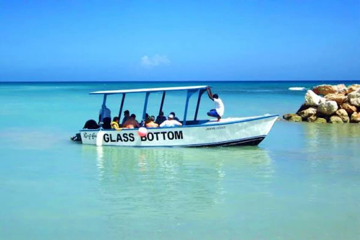 Glass bottom boat with tourists in clear turquoise water near rocky shore in Bali
