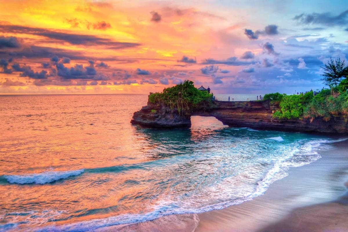 Tanah Lot temple at sunset with golden sky, ocean waves, and rocky coastal formation in Bali, Indonesia