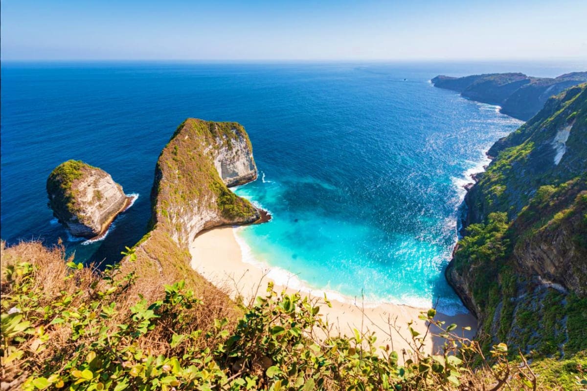 Aerial view of Kelingking Beach in Bali with turquoise waters, white sand cove, and dramatic limestone cliffs surrounded by t