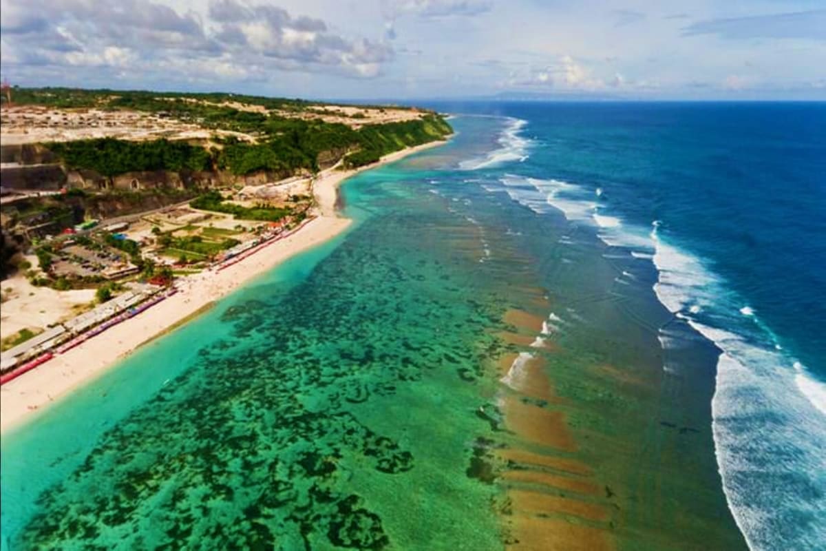 Aerial view of Bali's Uluwatu cliffside beach with turquoise waters, white sand, and lush green vegetation overlooking the In