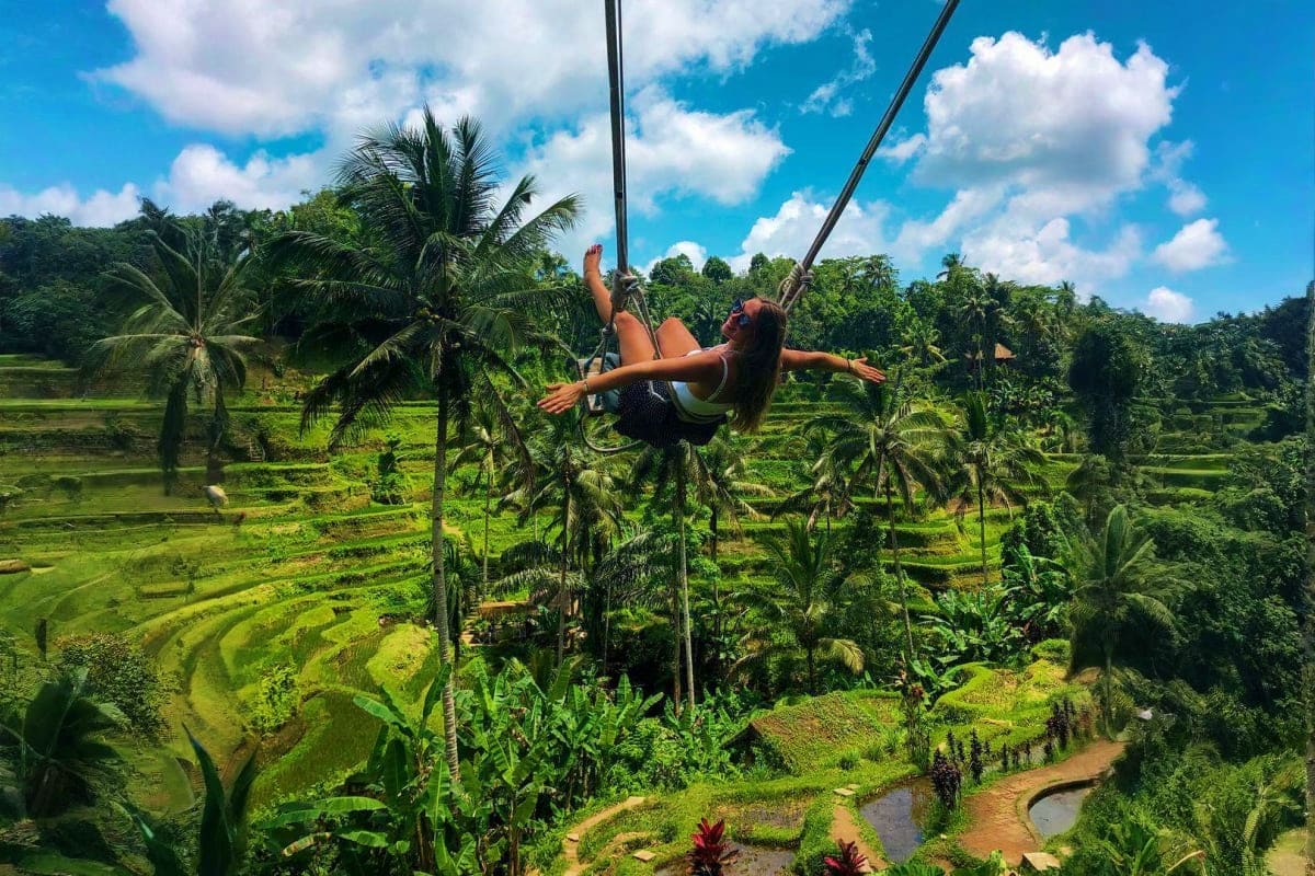Woman on rope swing over lush green rice terraces and tropical jungle landscape in Bali