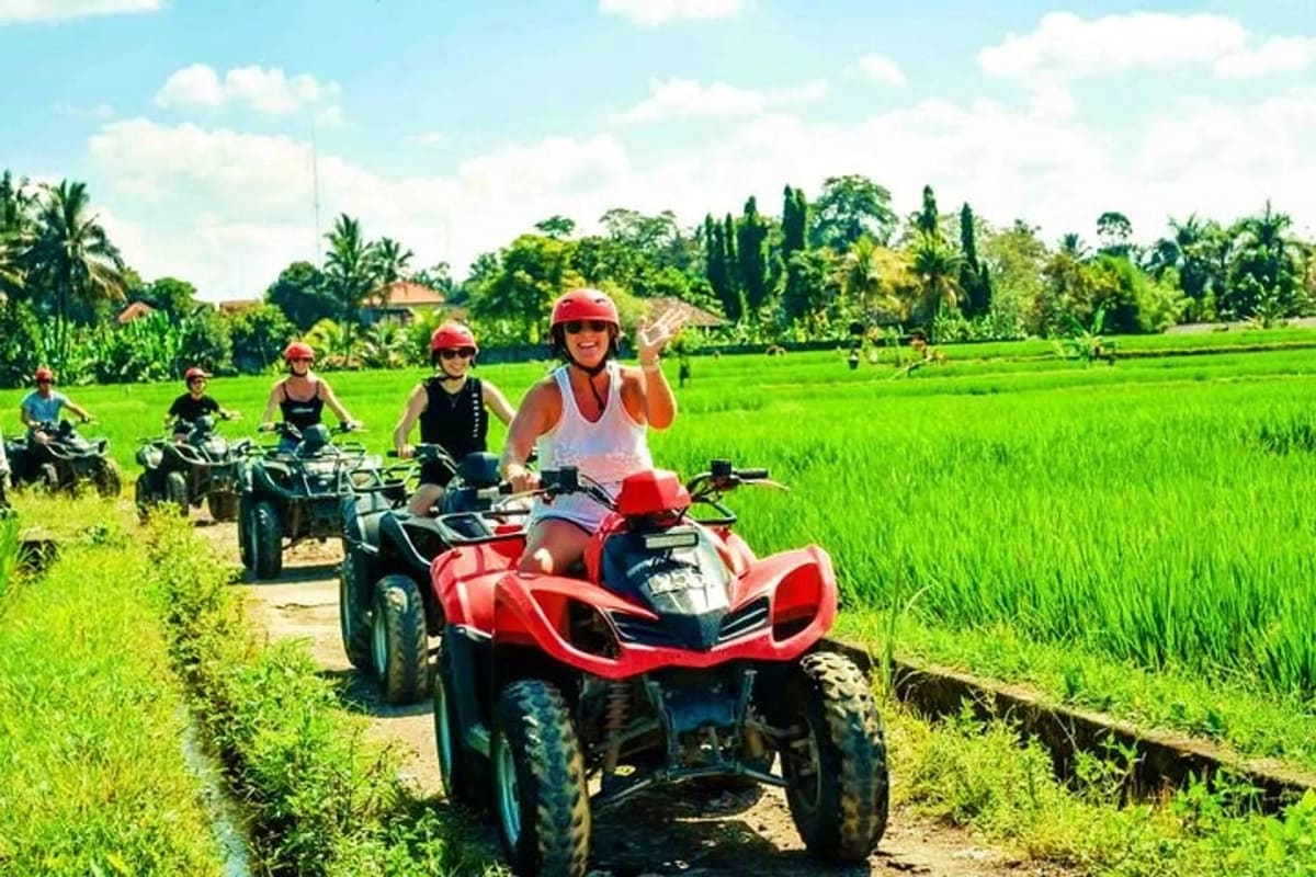 Group of tourists riding red ATVs through lush green rice paddies in Bali during daytime tour