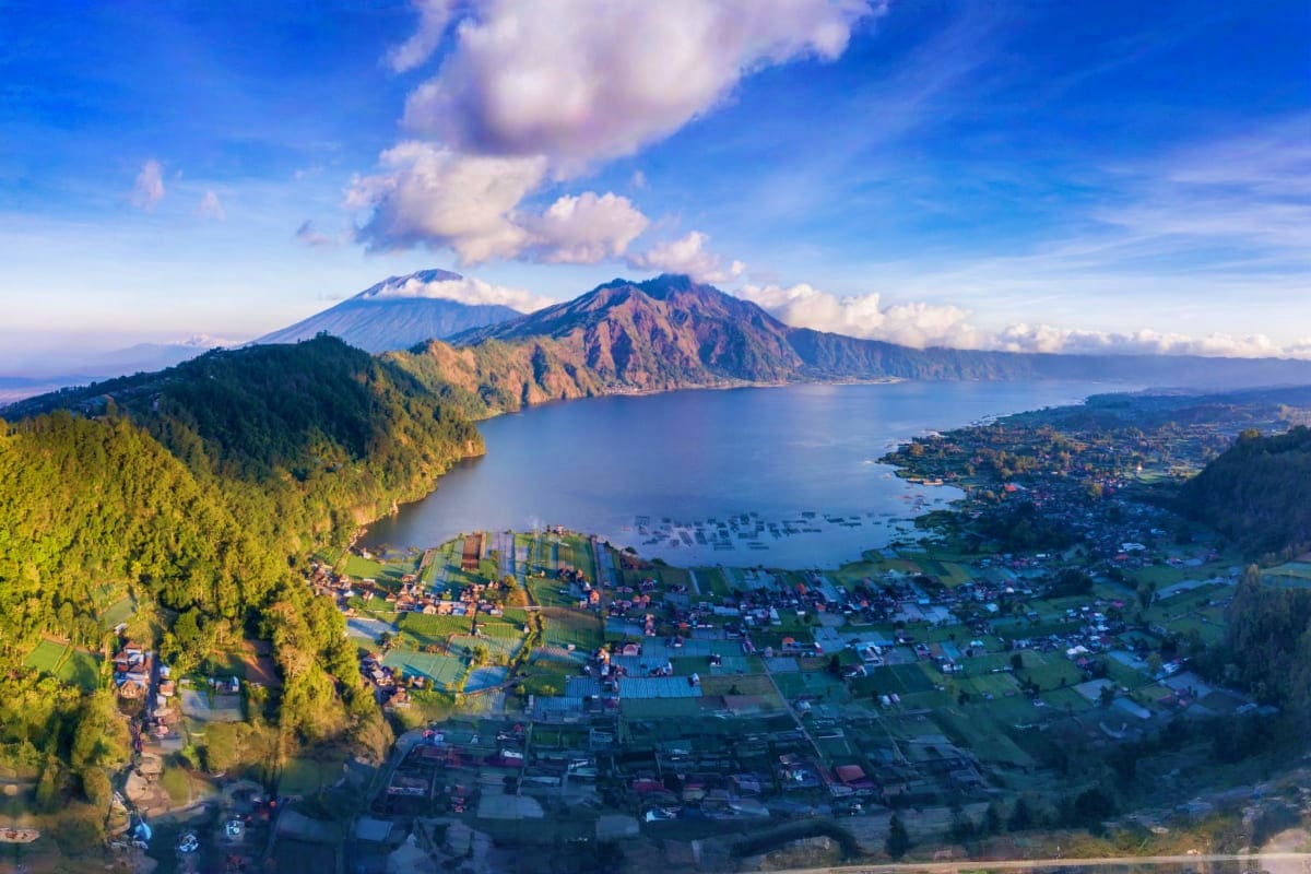 Aerial view of Lake Batur with volcanic mountains, forested slopes, and village settlements in Bali, Indonesia