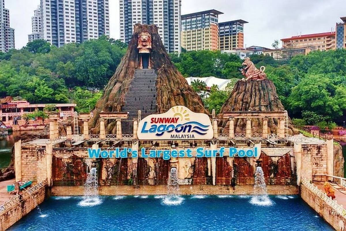 Sunway Lagoon water park entrance with massive tiki head sculptures and blue wave pool, surrounded by tropical greenery and h