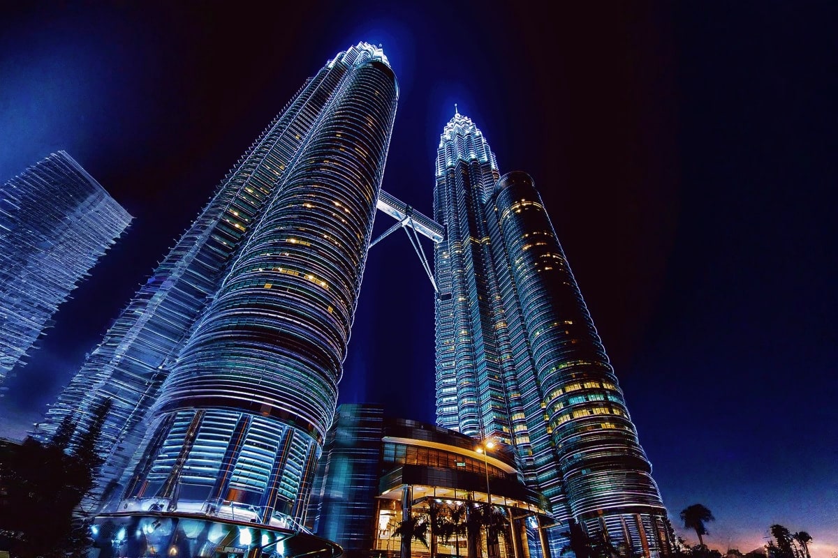Petronas Twin Towers illuminated at night in Kuala Lumpur, Malaysia with blue lighting and surrounding modern architecture ag