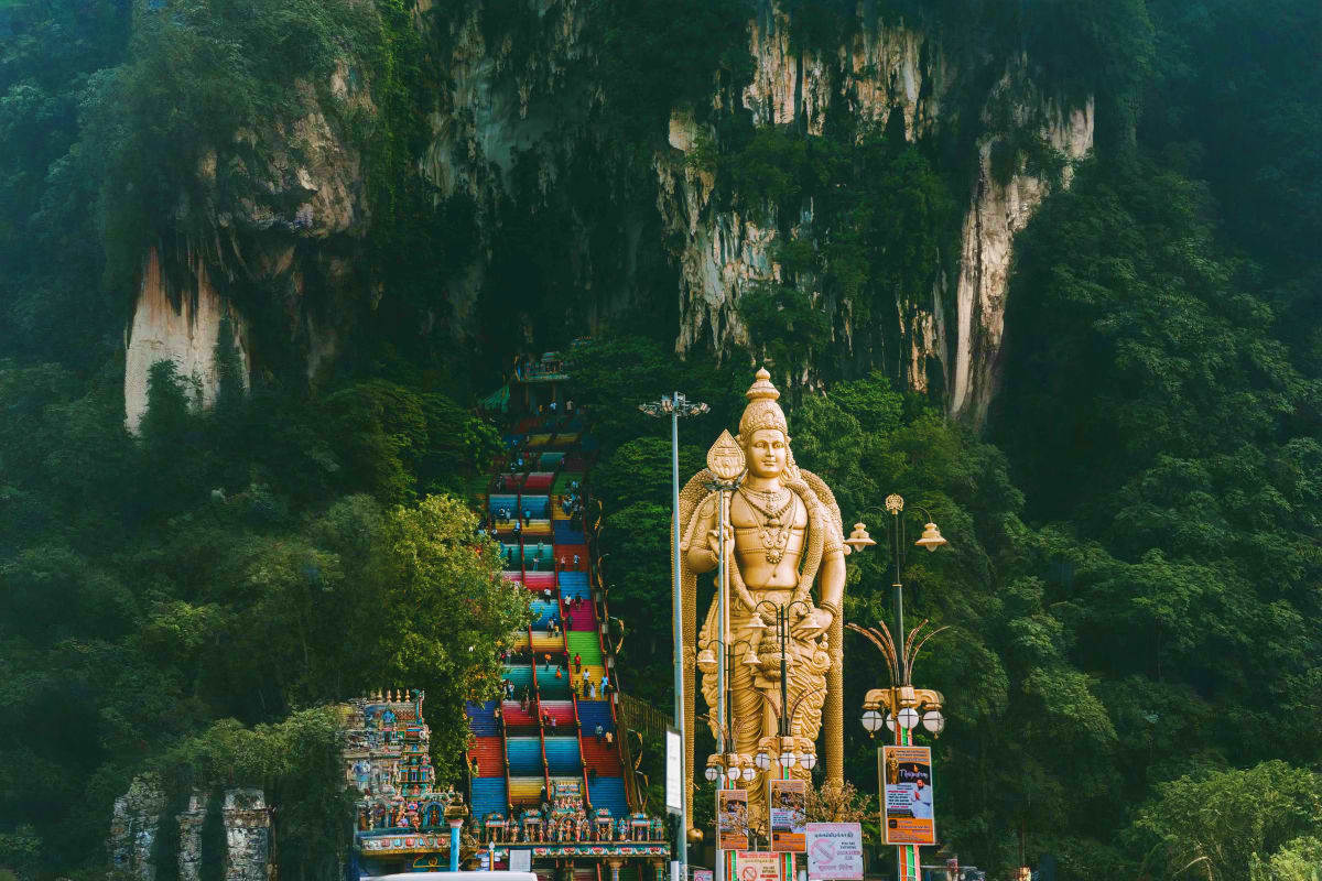 Golden Hindu deity statue at Batu Caves entrance with colorful staircase and limestone cliffs in Kuala Lumpur, Malaysia