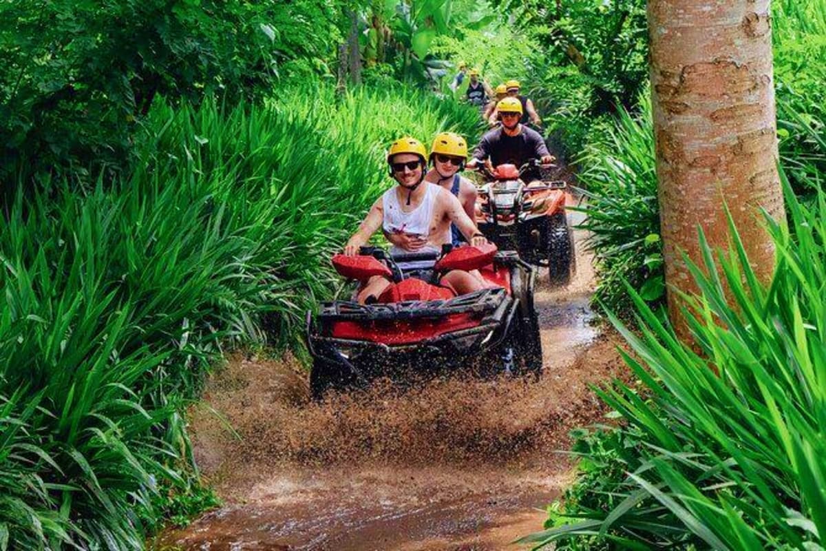 Group of tourists riding red and black ATVs through lush jungle vegetation on muddy trail in Bali