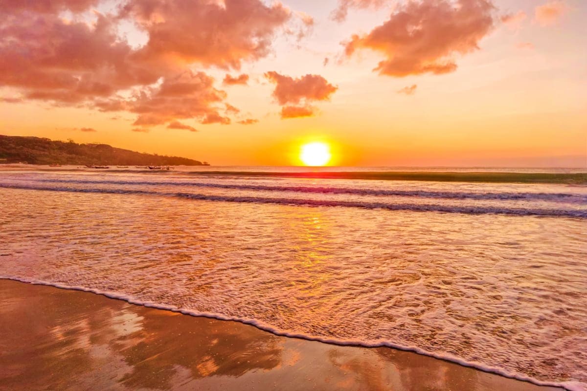 Golden sunset over ocean waves on tropical beach with hills in background