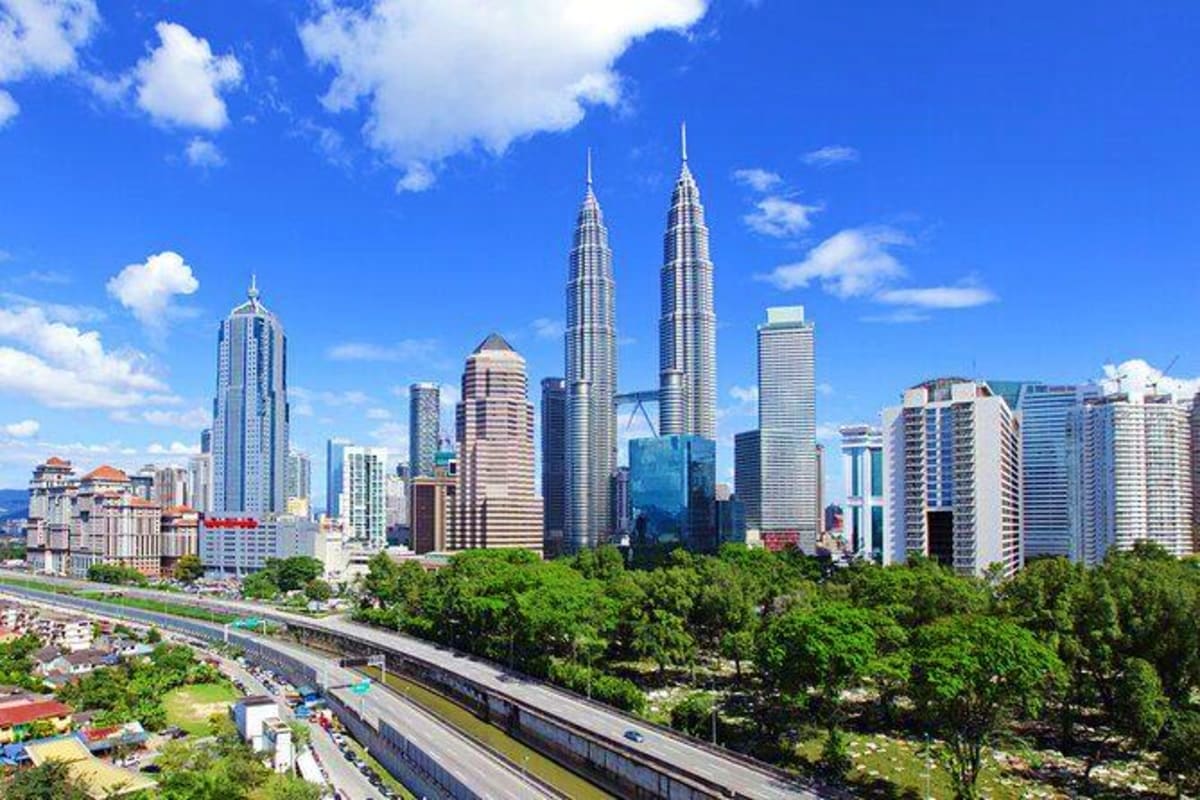 Kuala Lumpur skyline featuring the iconic Petronas Twin Towers and modern skyscrapers under a clear blue sky with green veget