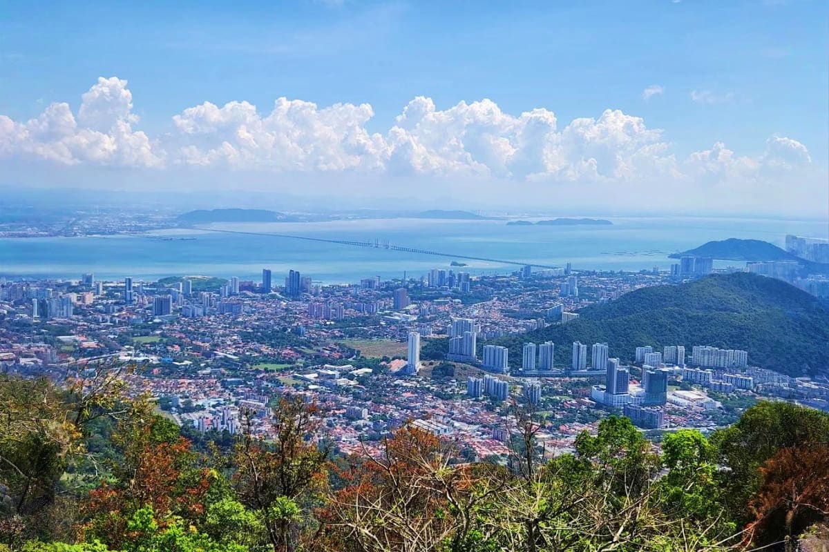 Aerial view of Penang cityscape with bridge spanning blue strait, mountains, and cloudy sky from elevated viewpoint